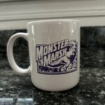 White coffee mug with purple graphic of a T-Rex, purple text that reads Monster Marsh.